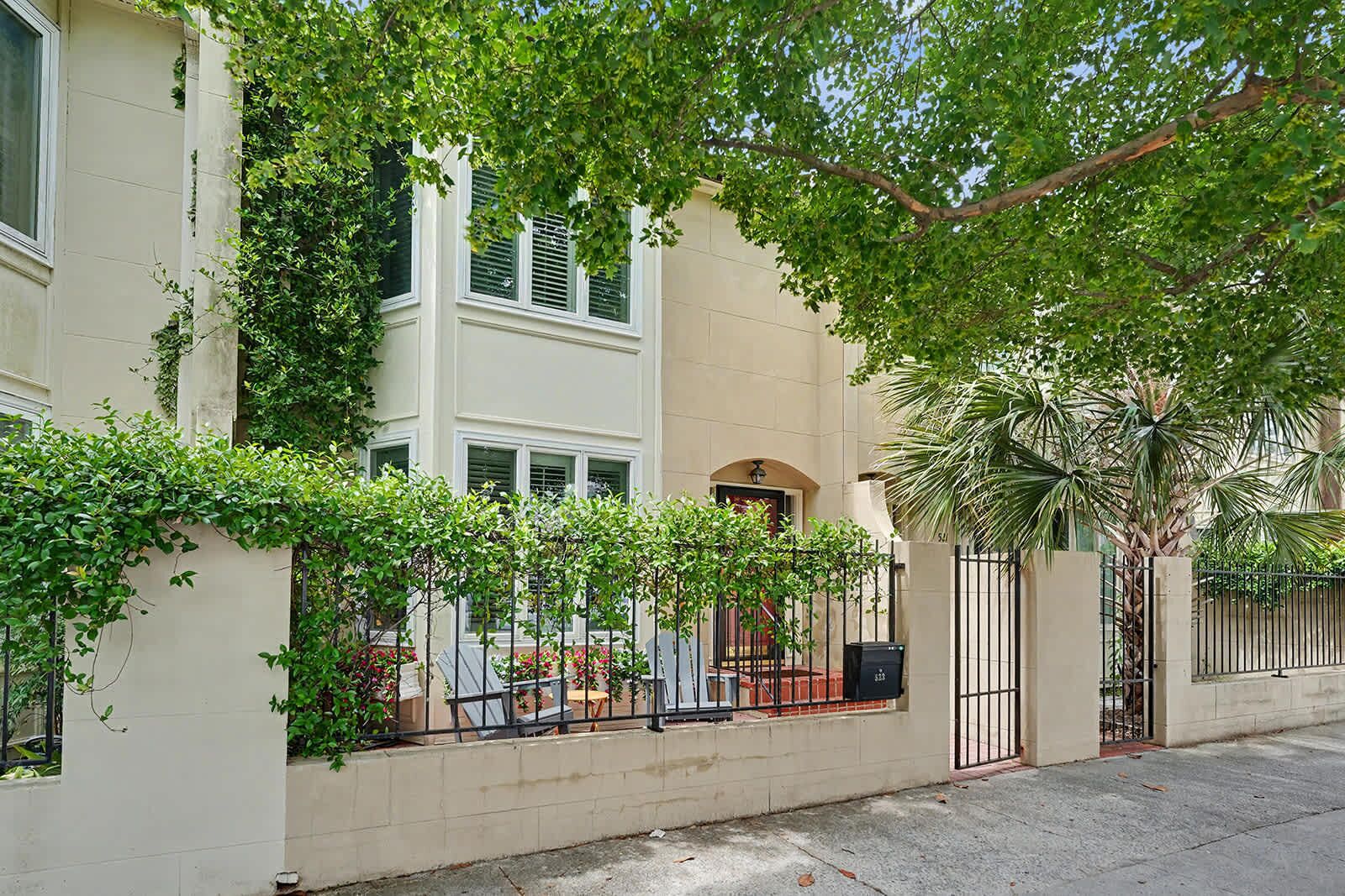 A two-story building with a white facade, a gated entrance, and a tree providing shade.