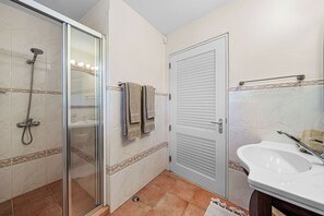 Ein Badezimmer mit Duschkabine aus Glas, einem weißen Waschbecken und einer Tür mit Handtuchhalter.