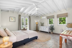 Ein Schlafzimmer mit einem Bett, Nachttisch, Lampe, Kommode, Fenstern und einem Deckenventilator.