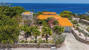 Um imóvel à beira-mar com um muro de pedra, entrada por um caminho pavimentado e vista para o oceano.