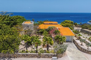 Une propriété située sur la côte, dotée d’un mur en pierre, d’un jardin avec différentes espèces de plantes et offrant une vue sur la mer.