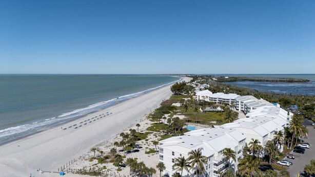 Ein Küstenhotel mit mehreren weißen Gebäuden, einem Sandstrand und freiem Blick auf den Ozean.