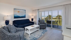 Ein modernes Wohnzimmer mit Sofa, Couchtisch und Sesseln, einem Gemälde an der Wand und einem Balkon mit Meerblick.