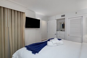 Une chambre d’hôtel avec un lit, une télévision, une armoire et une salle de bain visible à travers une porte ouverte.