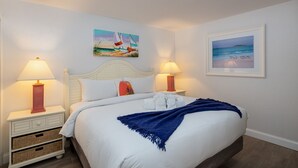 Ein ordentlich bezogenes Bett mit weißen Leinen und einer blauen Tagesdecke, zwei Nachttische mit Lampen, ein Kopfteil und zwei Bilder an der Wand.