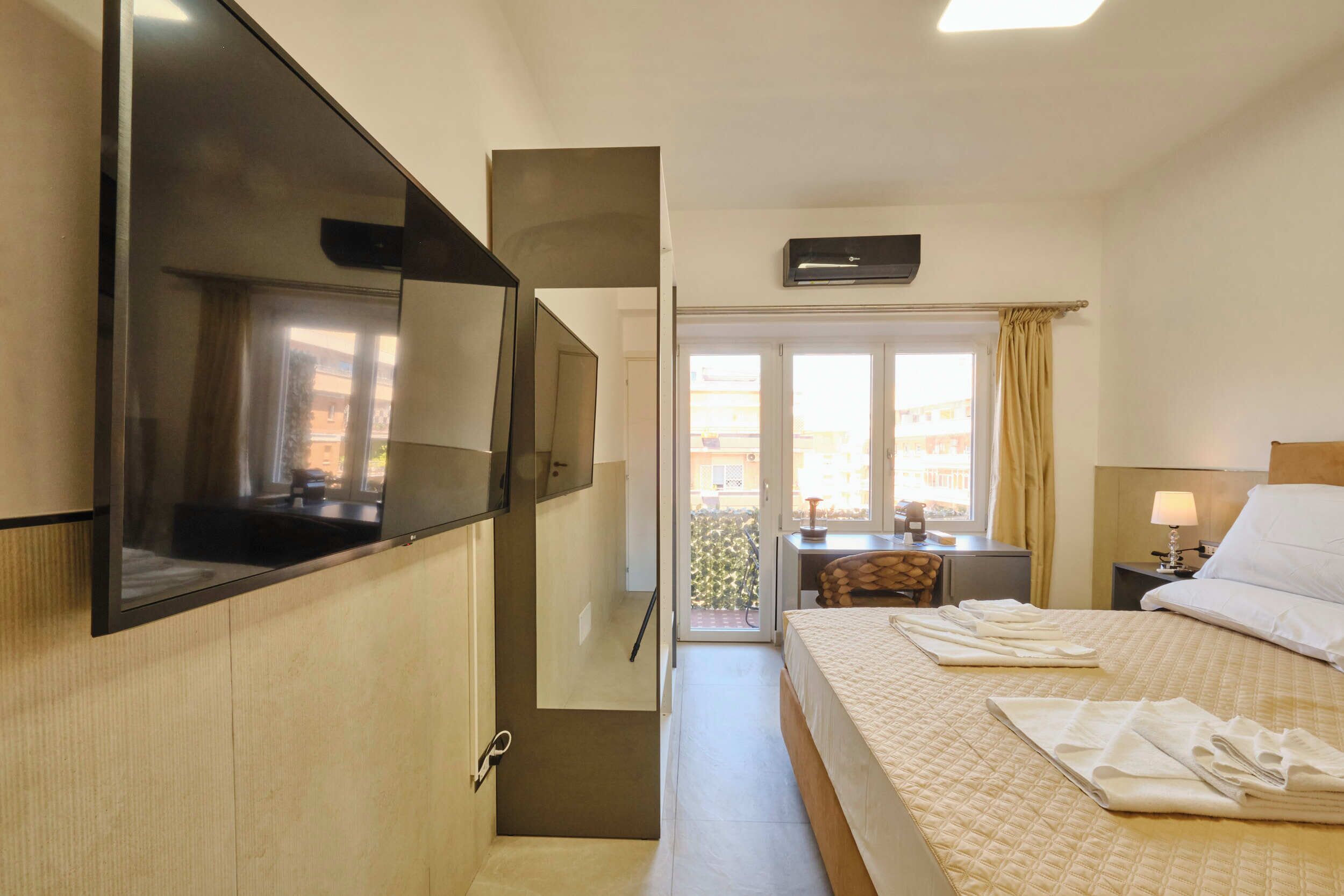 Ein Hotelzimmer mit Bett, einem an der Wand befestigten Fernseher, einem Schreibtisch mit Lampe und Blick durch die Tür.