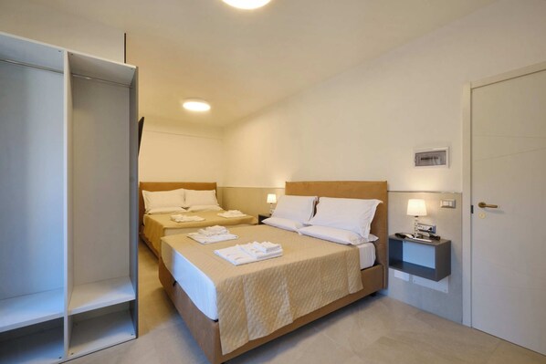 Una habitación de hotel con dos camas, un armario, una mesita de noche con lámpara y una puerta.