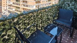 Un balcón con vista a un edificio de varios pisos, un muro verde y mobiliario exterior.