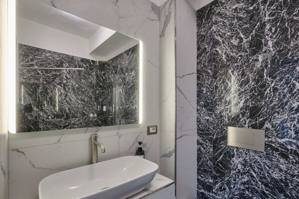 Un baño con lavamanos blanco, un espejo grande y paredes de mármol.