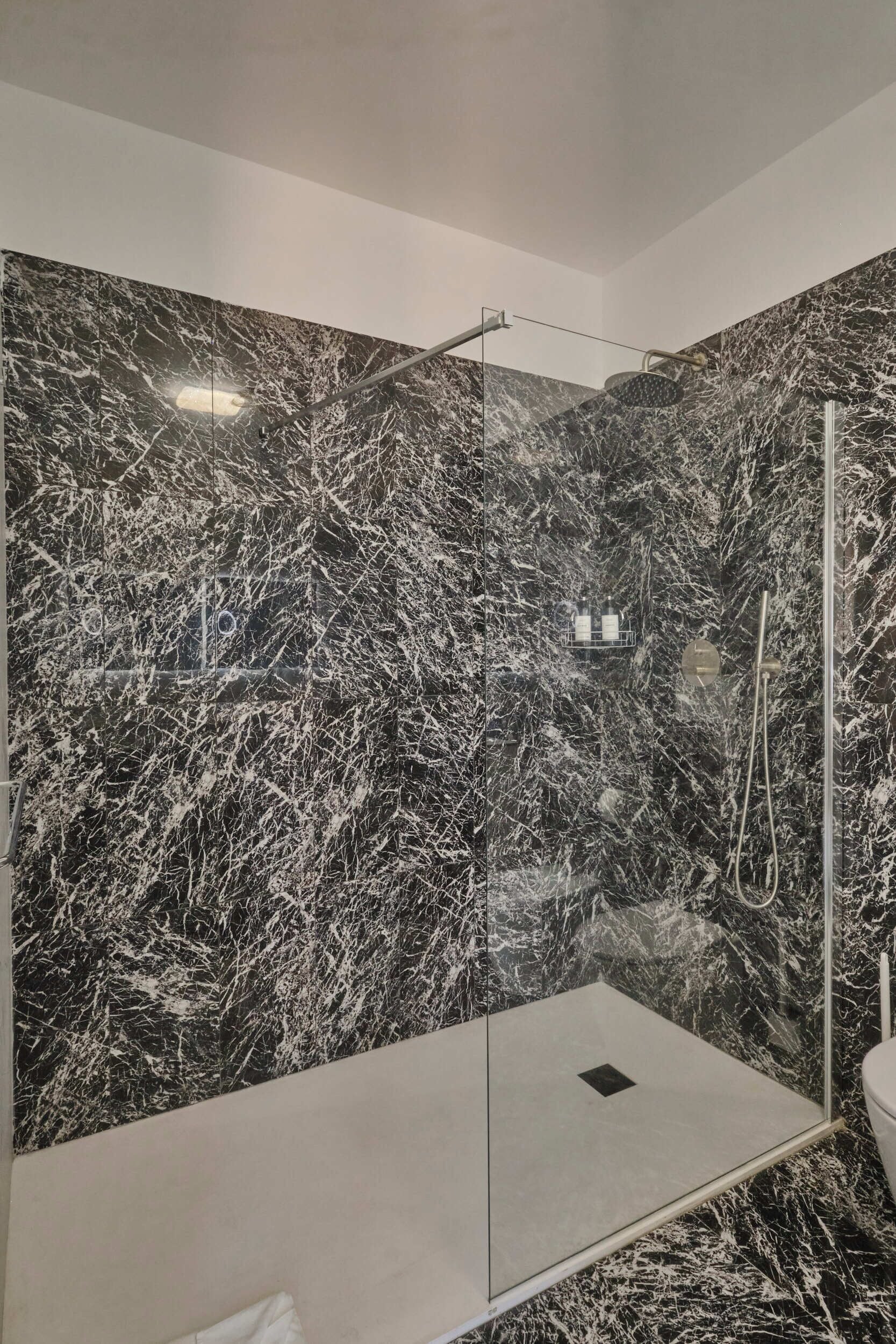 Ein modernes Badezimmer mit Duschkabine aus Glas, Marmorwänden und sichtbarer Toilette.