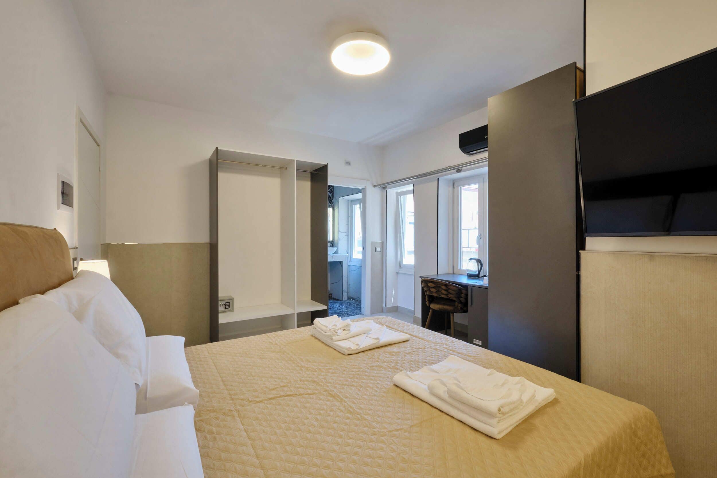 A hotel room with a bed, a desk, a chair, a mirror, and a door leading to a bathroom.