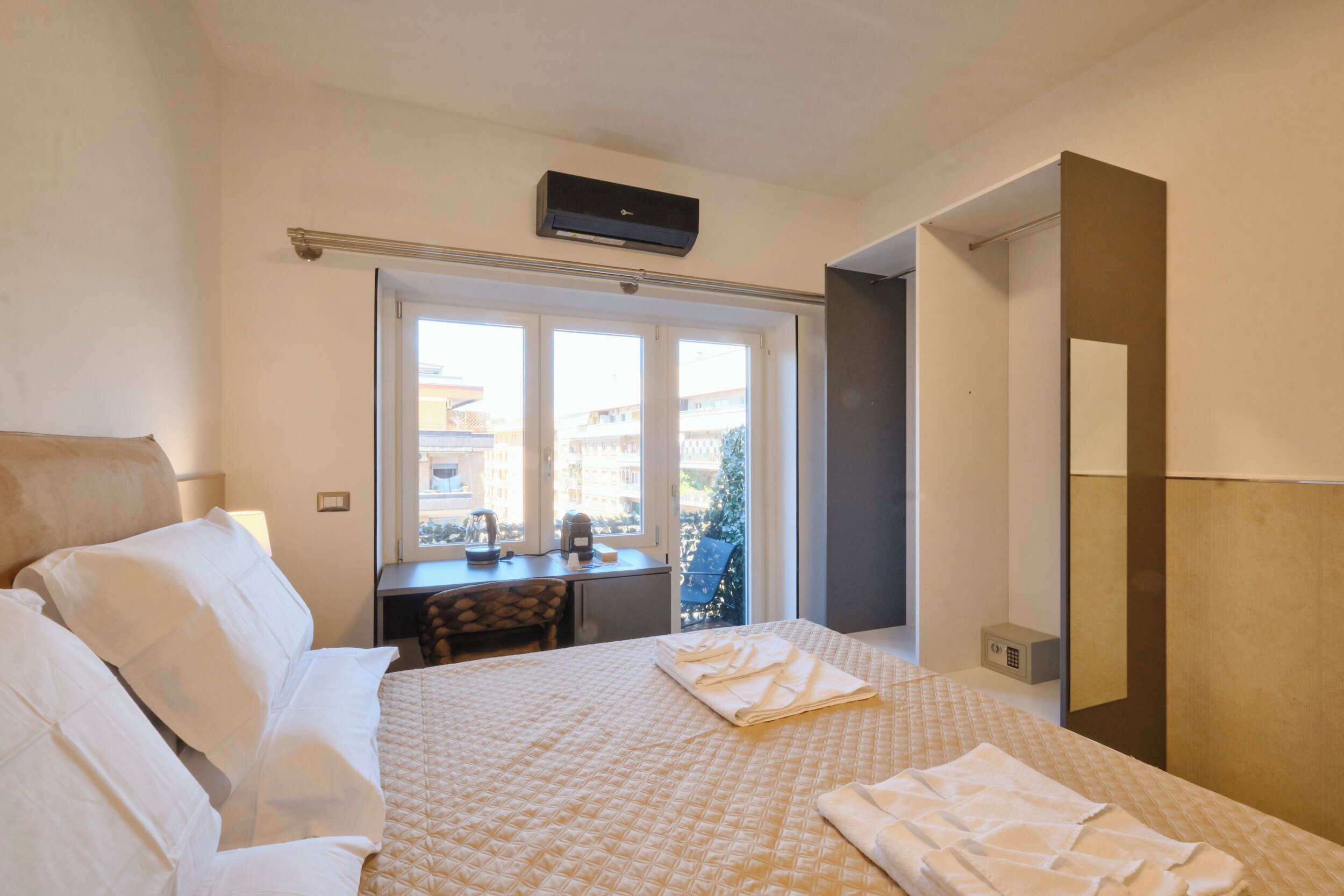 A hotel room with a bed, a desk, a chair, and a window with a view of buildings.