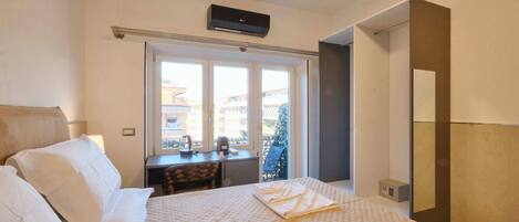 A hotel room with a bed, a desk, a chair, and a window with a view of buildings.