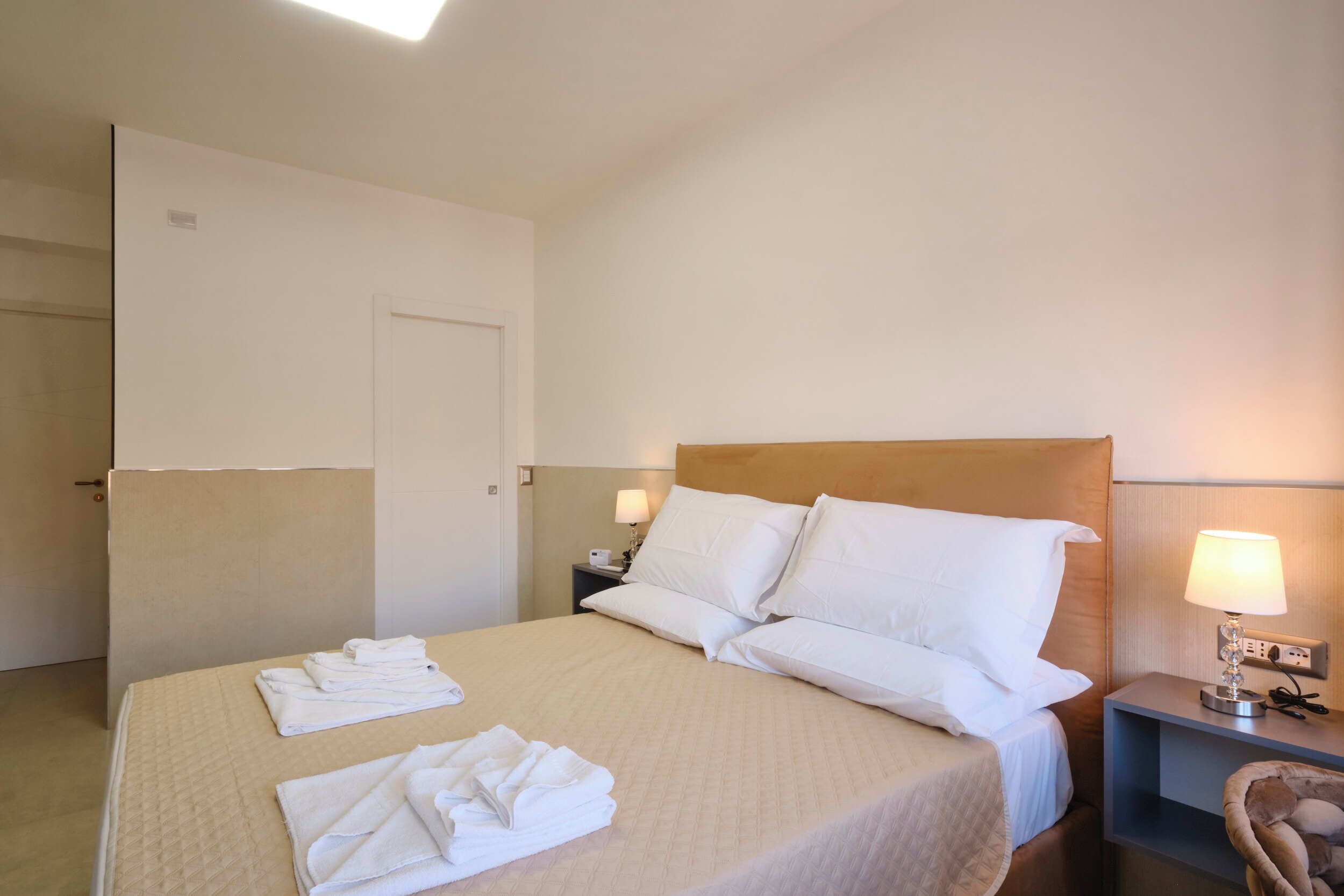 A hotel room with a bed, two bedside tables, a chair, and a door.