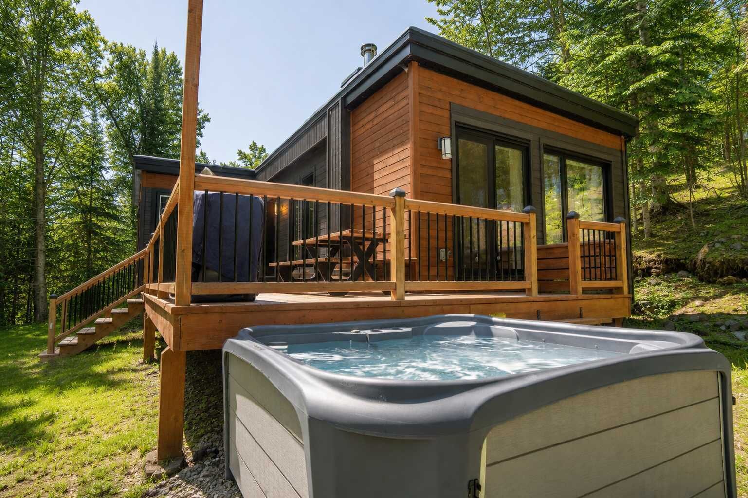 A cabin with a hot tub, wooden deck, and a staircase leading to the entrance.