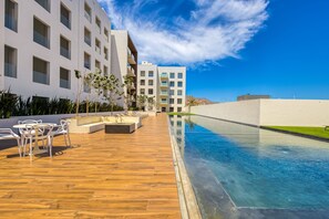 A modern hotel with a pool area, outdoor seating, and a view of the mountains. - Spacious Condo With Private Washer/dryer, City Views, and Shared Pool (Cabo San Lucas)