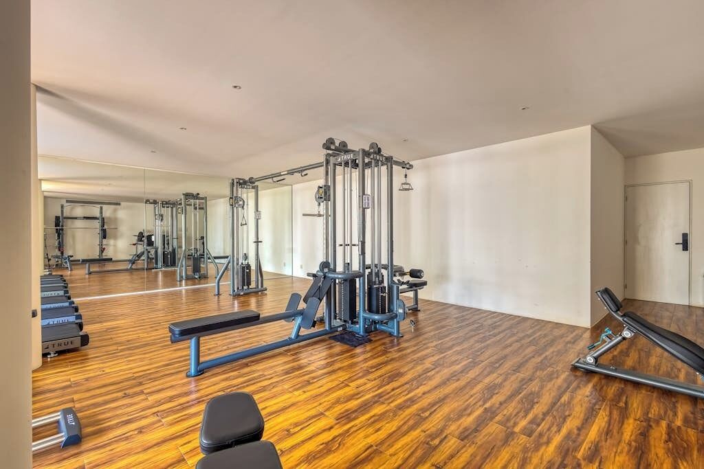 A gym with exercise equipment, wooden flooring, and a large mirror.