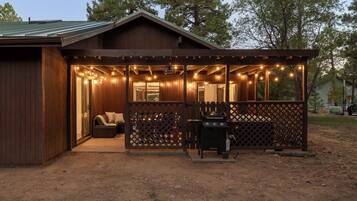 Eine Holzhütte mit überdachter Veranda, Grill und Sitzgelegenheit.