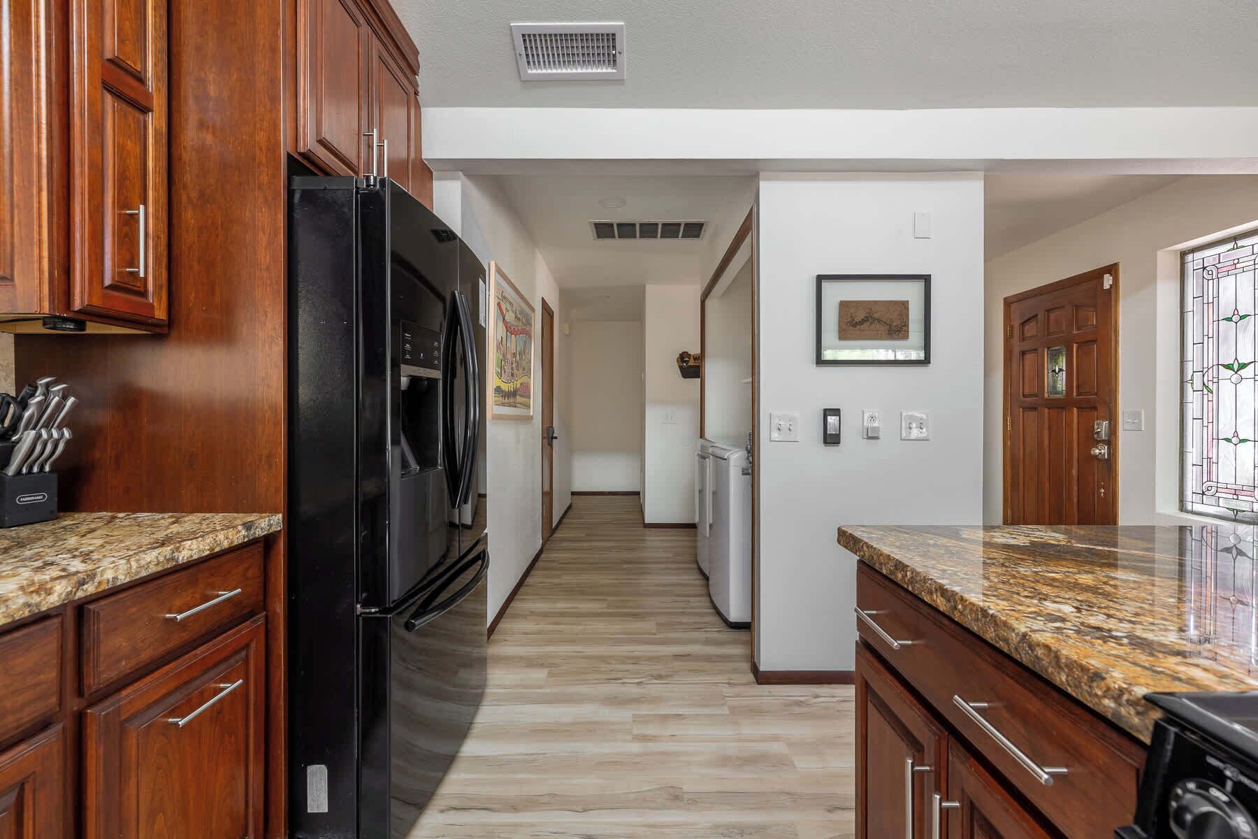 A kitchen with wooden cabinets, a black refrigerator, a microwave, and a granite countertop.