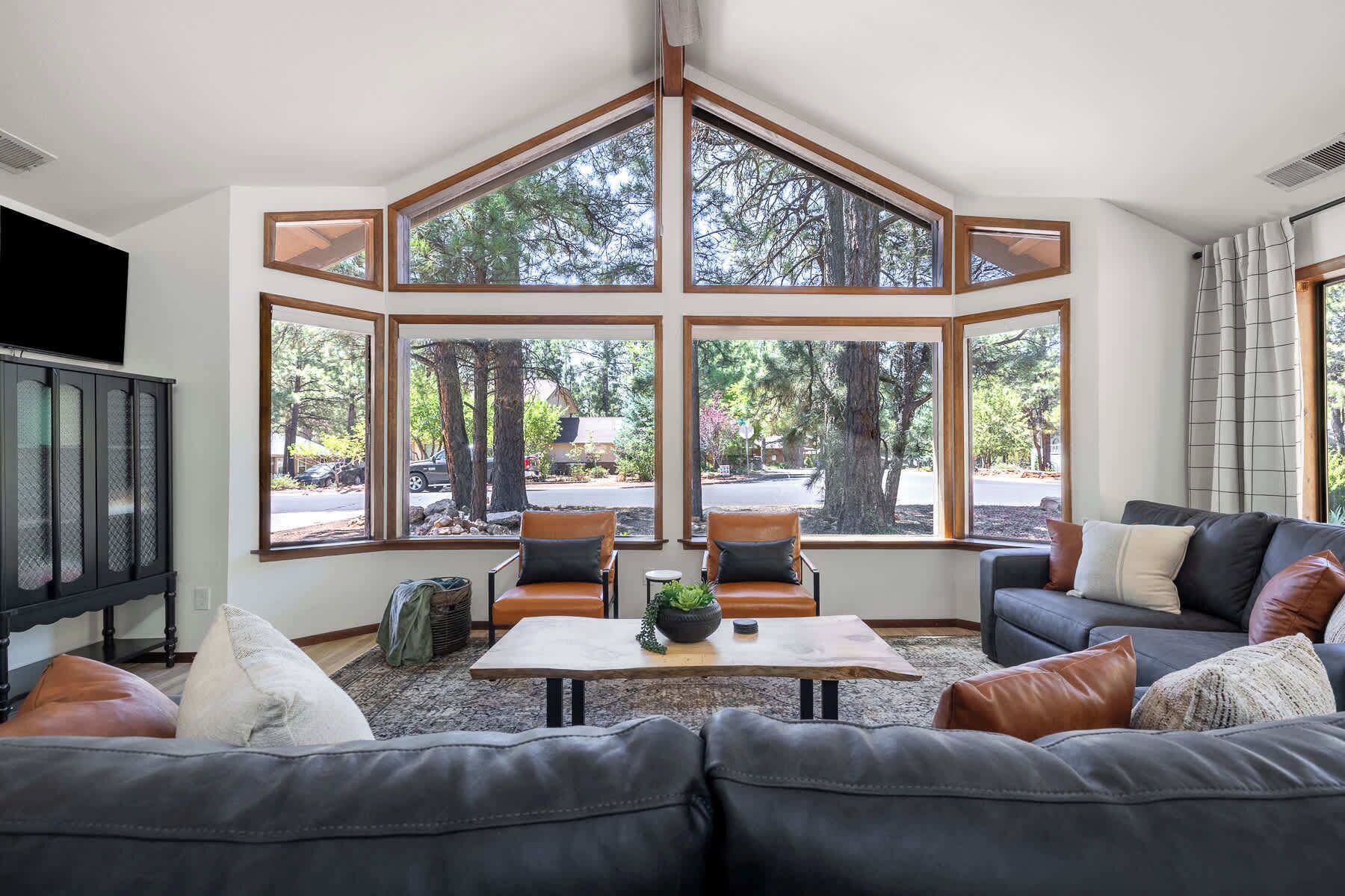 A living room with a large bay window, two chairs, a sofa, a coffee table, and a television.
