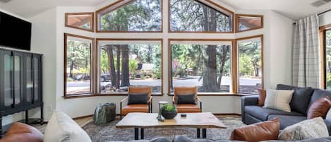 A living room with a large bay window, two chairs, a sofa, a coffee table, and a television.