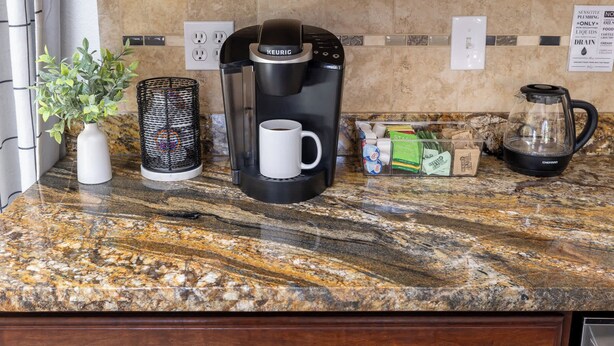 Eine Küchenarbeitsplatte mit einer Keurig-Kaffeemaschine, einer Kaffeetasse, einer Pflanze, einem Mülleimer und einer Kapselbox.