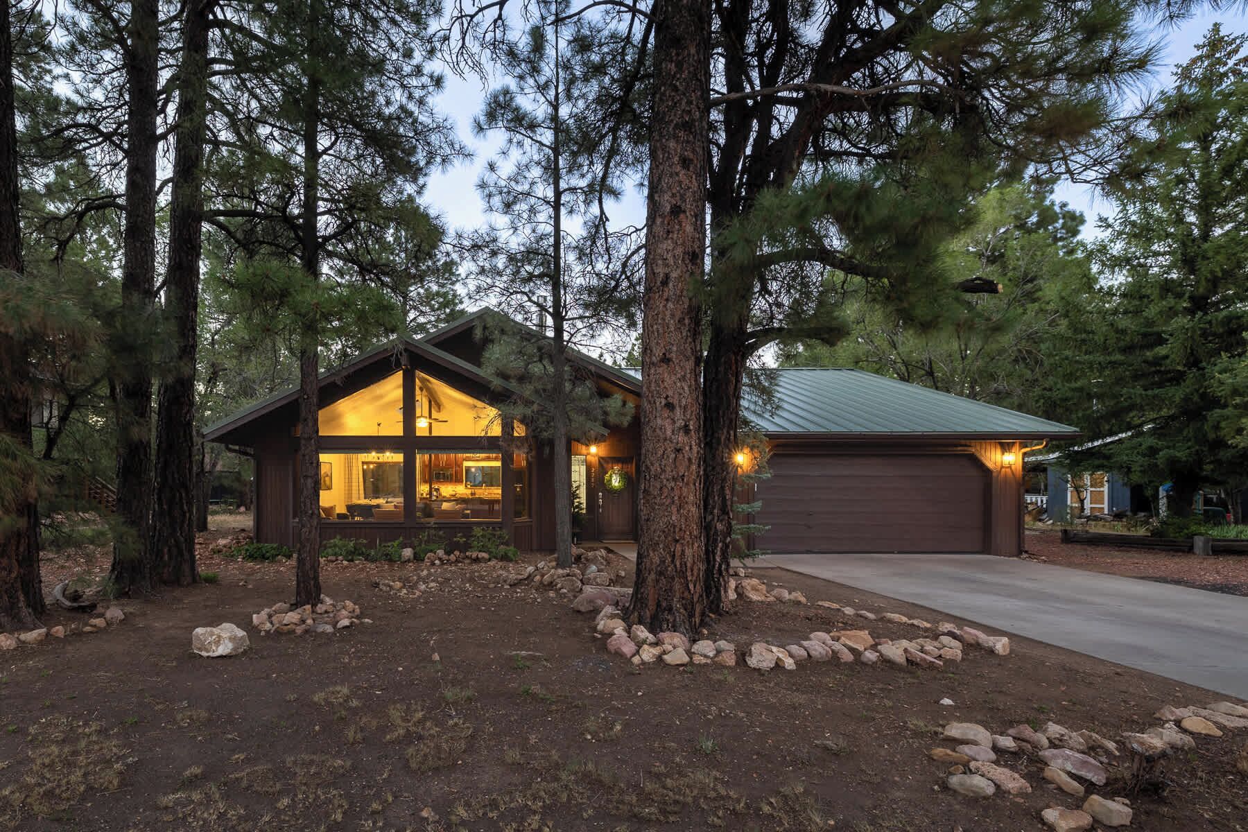 A cabin with a large glass window, a garage, and a well-maintained garden with rocks.