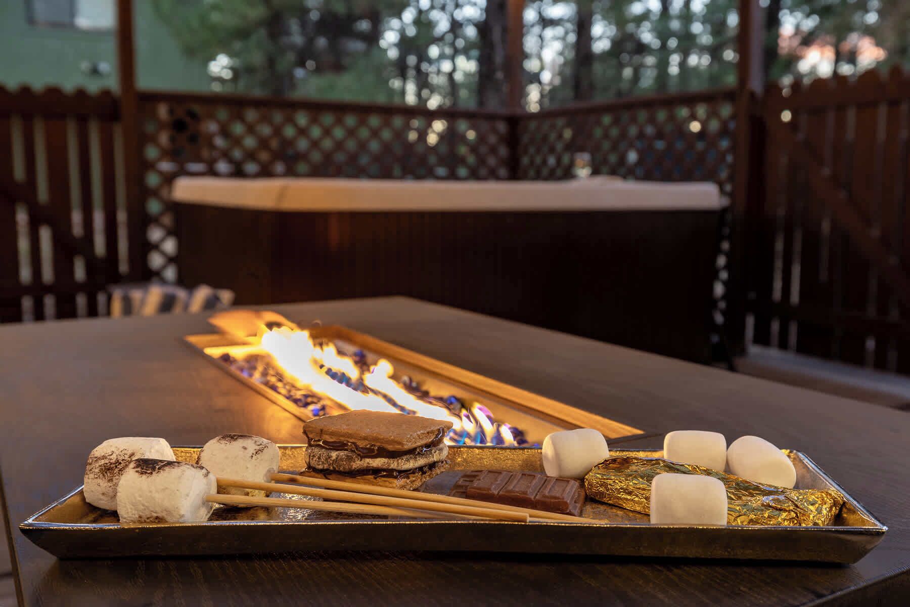 A tray of food items including marshmallows, chocolate, and ice cream, placed on a table with a fire in the background.