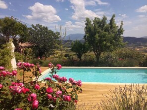 A pool with a wooden deck, surrounded by lush greenery and flowering plants. - Apartment 'La Roseraie Des Côtes' with Private Pool, Private Garden and Wi-Fi (Vinsobres)