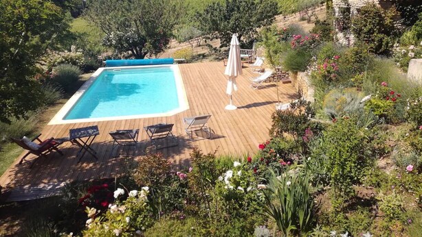 Una piscina rectangular con muelle de madera, rodeada de exuberante follaje y flores.