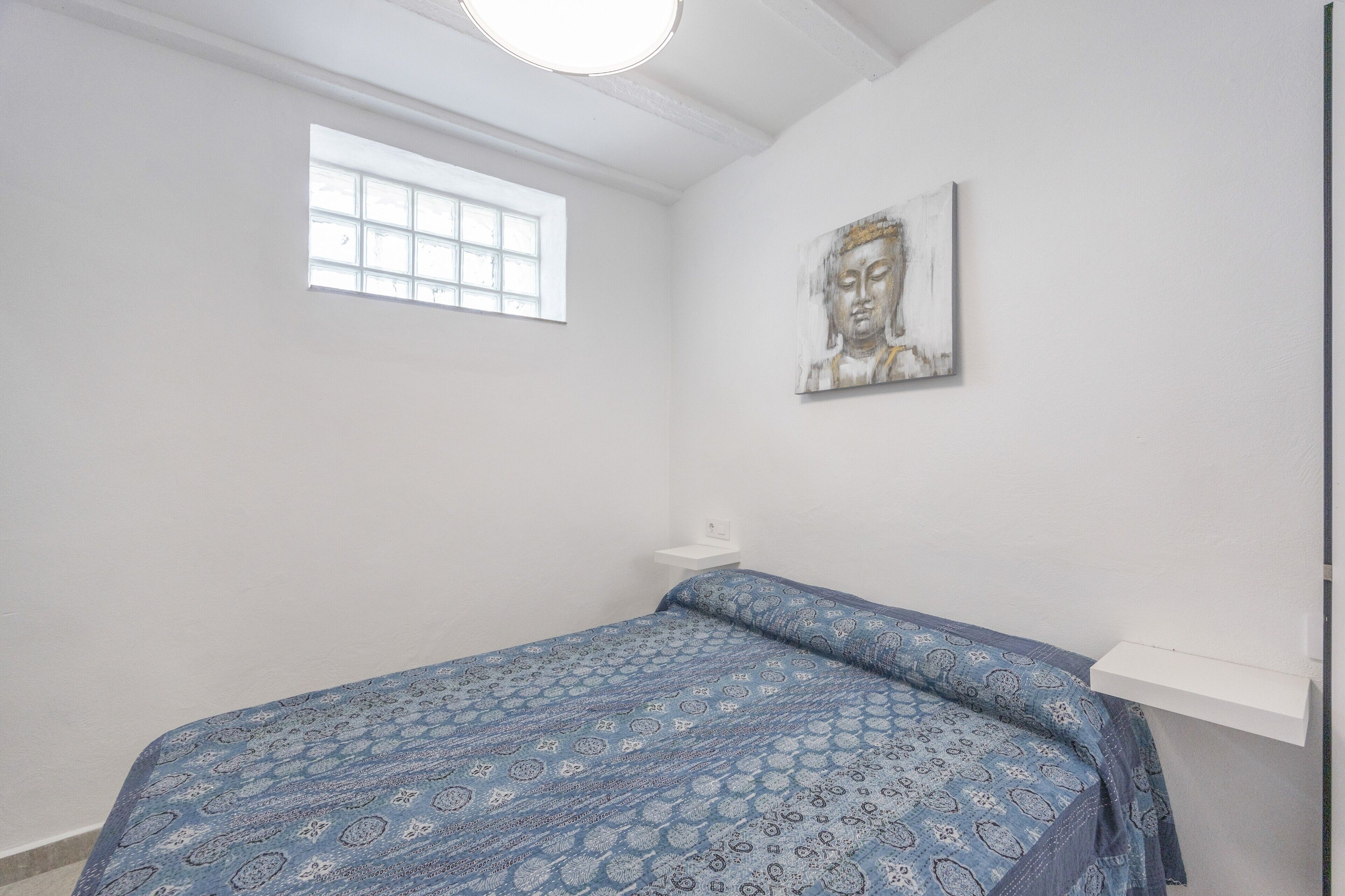 Een slaapkamer met een bed, een raam en een kunstwerk aan de muur.