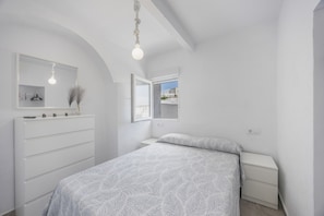 Een slaapkamer met een bed, een dressoir, een nachtkastje, een spiegel en een raam.