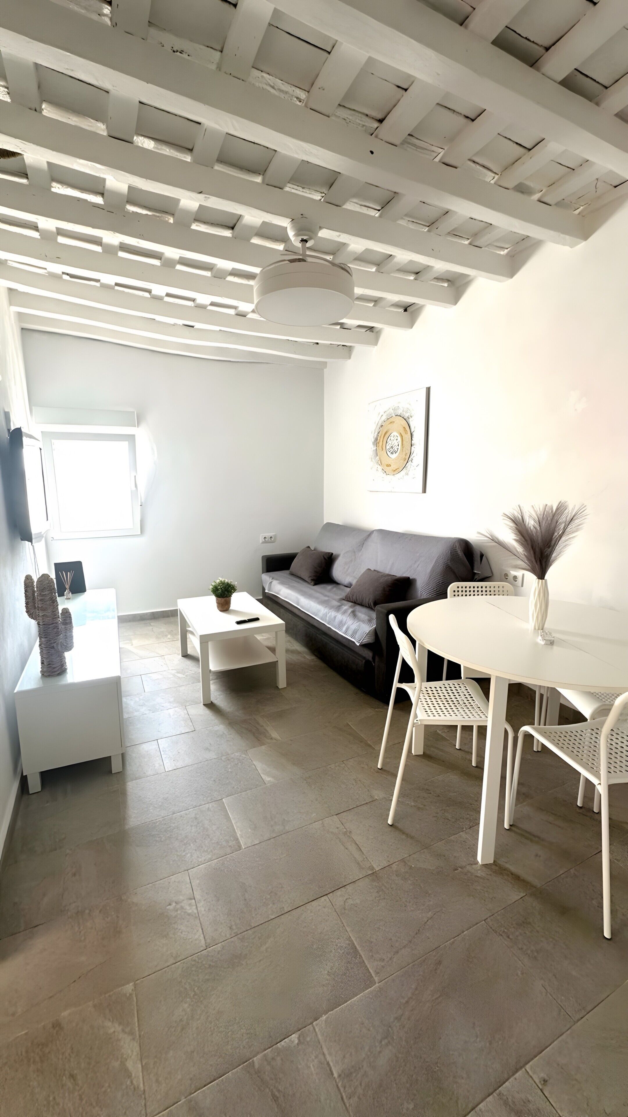 A modern living room with a grey sofa, white coffee table, and a dining area with white chairs and a table.. 'La Joyita Del Centro' Apartment with Shared Garden and Wi-Fi