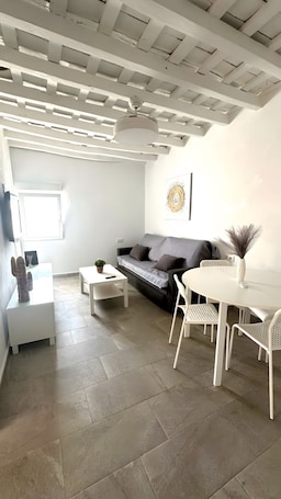 A modern living room with a grey sofa, white coffee table, and a dining area with white chairs and a table.. 'La Joyita Del Centro' Apartment with Shared Garden and Wi-Fi