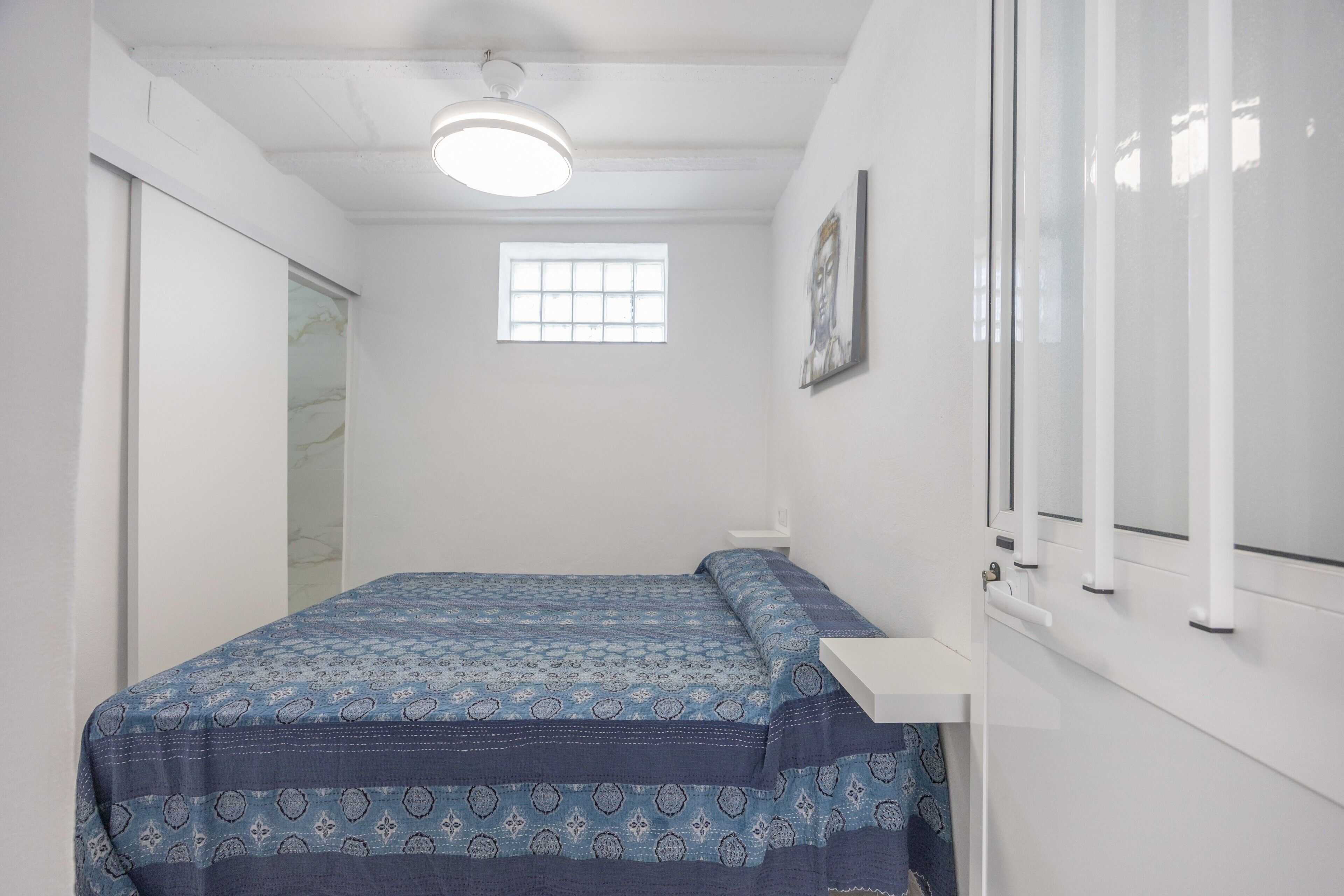 A bedroom with a bed, a window, a ceiling light, and a door.
