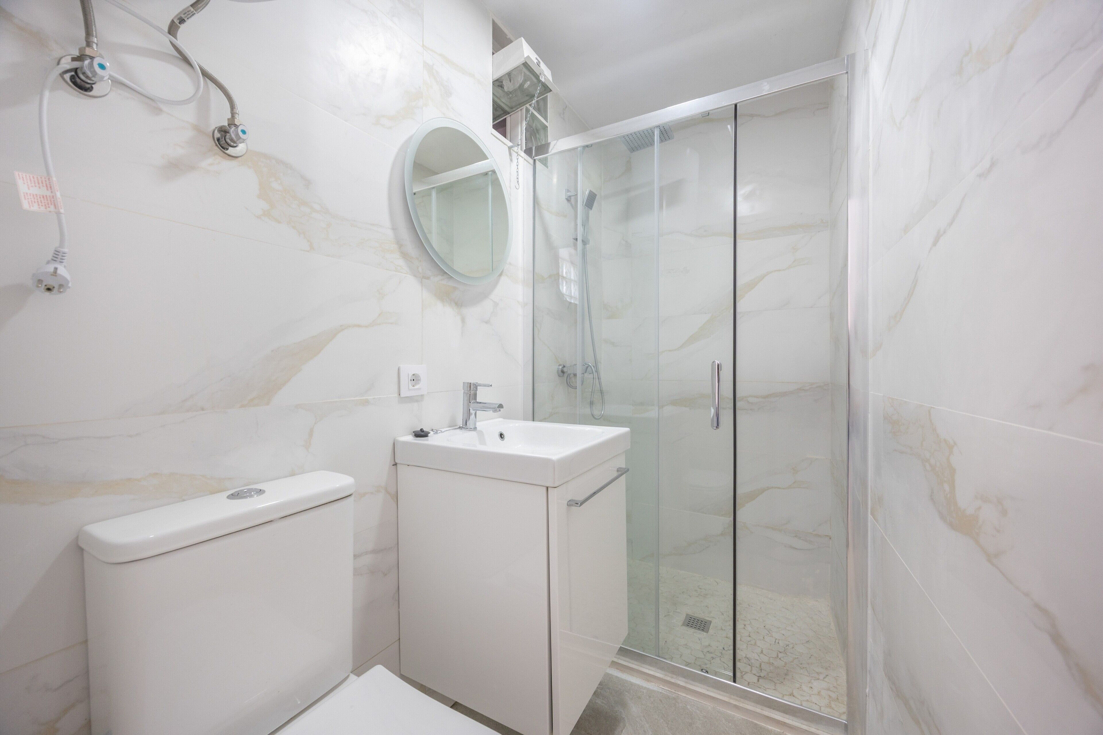 A bathroom with a toilet, sink, mirror, and glass-enclosed shower.