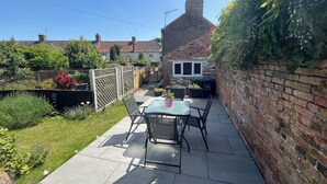 A patio with a table and chairs, a brick wall, and a garden with various plants. - Copper Cottage – Charming Central Devizes Retreat with Secluded Garden (Devizes)