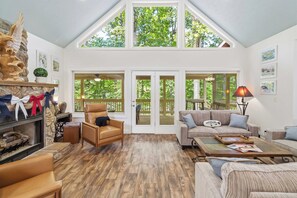 A spacious living room with a high ceiling, large windows, and a fireplace.