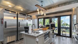 Een moderne keuken met roestvrijstalen apparatuur, een granieten aanrechtblad en uitzicht door grote schuifdeuren.