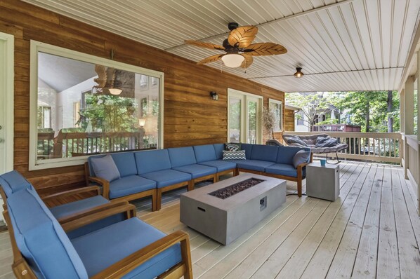 A covered outdoor seating area with a wooden deck, blue cushioned seating, and a ceiling fan.