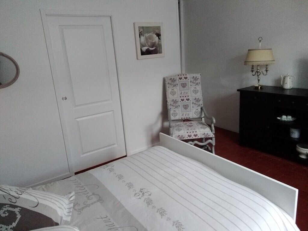 Een slaapkamer met een bed, een stoel, een kaptafel, een lamp en een foto aan de muur.