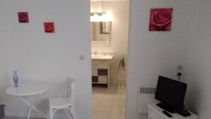 Une pièce comprenant un lit, une petite table avec une chaise, un téléviseur posé sur un meuble, et une salle de bain visible à travers une porte ouverte.