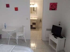 Quarto com uma cama, uma mesinha com cadeira, uma televisão em um móvel e um banheiro visível por uma porta aberta.