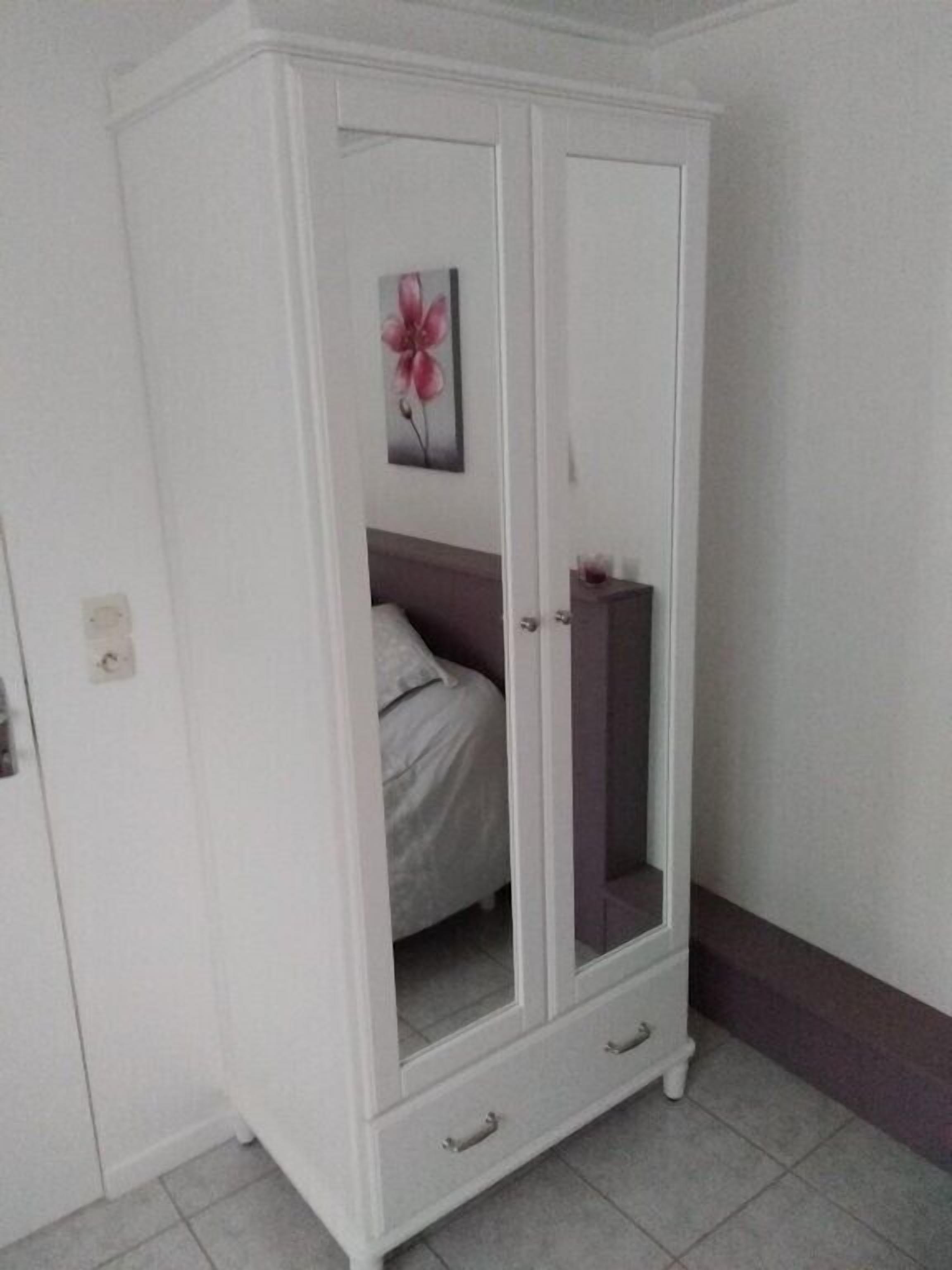 A white wardrobe with a mirror, a bed with a headboard, and a wall-mounted artwork.