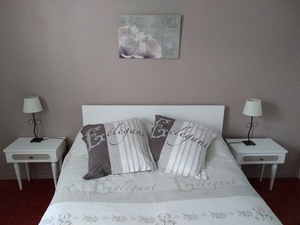 Ein ordentlich bezogenes Bett mit Kissen mit der Aufschrift 'Elegant', zwei Nachttische mit Lampen, ein Wandbild und ein Teppichboden.