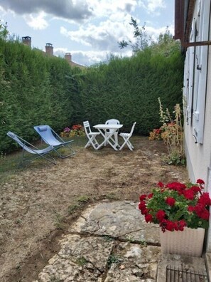 Eine Terrasse mit einem Kiesweg, weißen Gartenmöbeln und einer Hecke im Hintergrund.