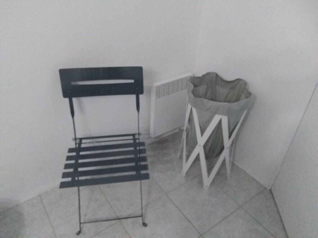 A corner with a metal chair, a white radiator, and a white trash bin.
