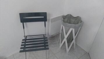A corner with a metal chair, a white radiator, and a white trash bin.