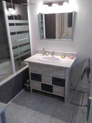 Ein Badezimmer mit Duschkabine aus Glas, einem weißen Waschbecken, einem Spiegel und Fliesenboden.