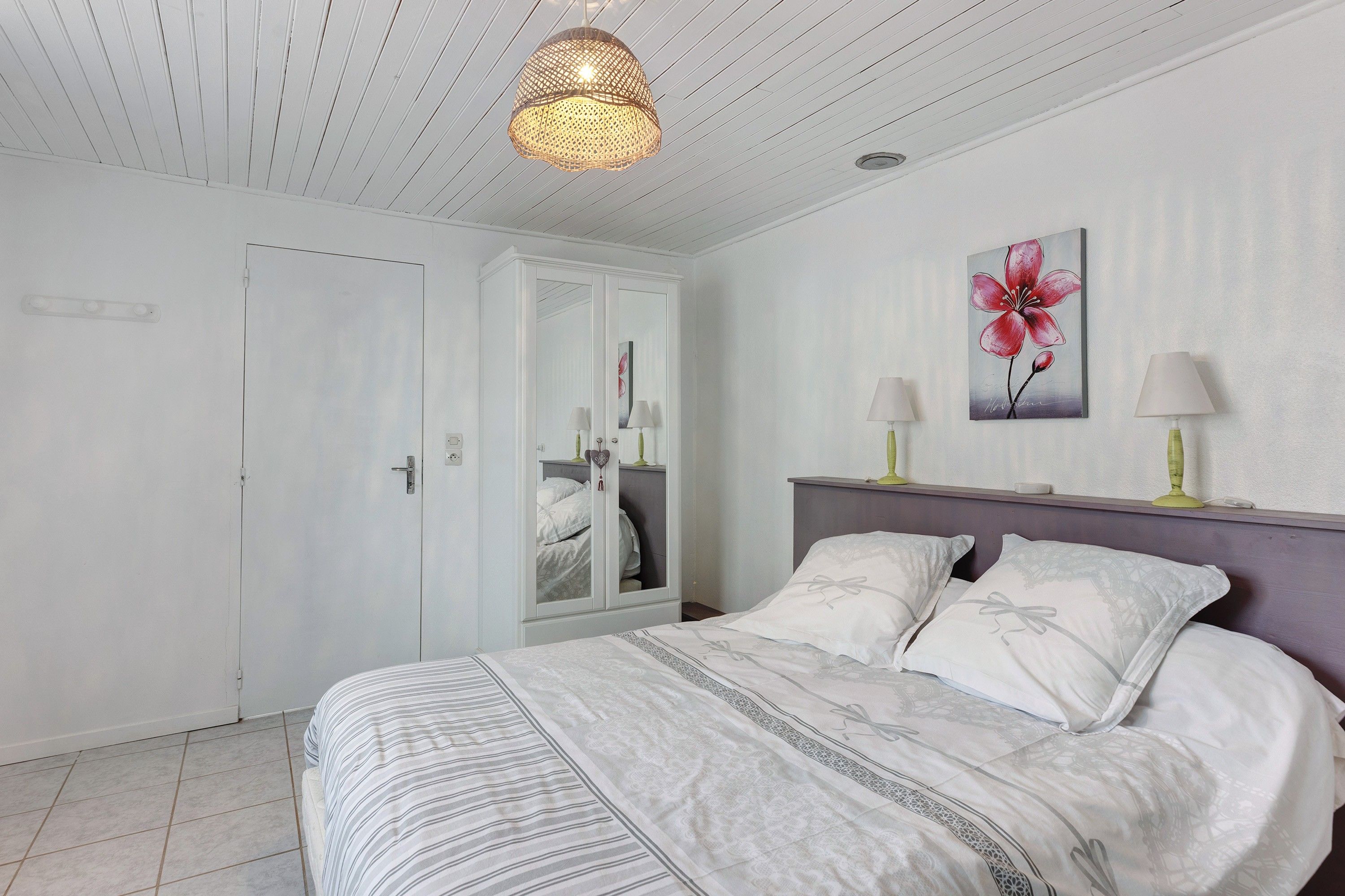 Een slaapkamer met een bed, nachtlampjes, een spiegel en een aan de muur hangend kunstwerk.